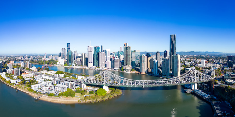 A panoramic aerial view of the Brisbane skyline with the Story Bridge under a clear blue sky